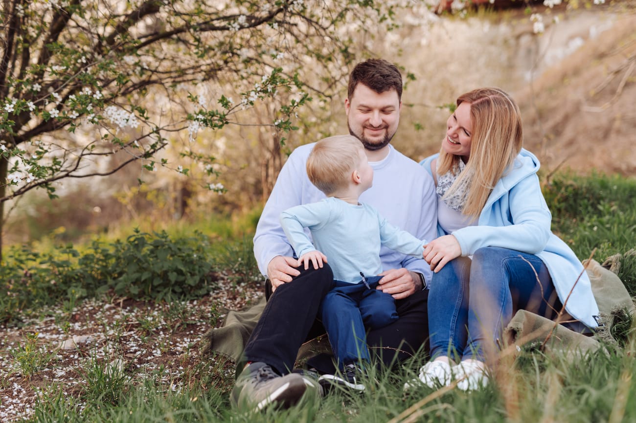 Dziecko wpatrzone w rodziców, którzy siedzą obok niego i się uśmiechają - rodzinna sesja zdjęciowa.