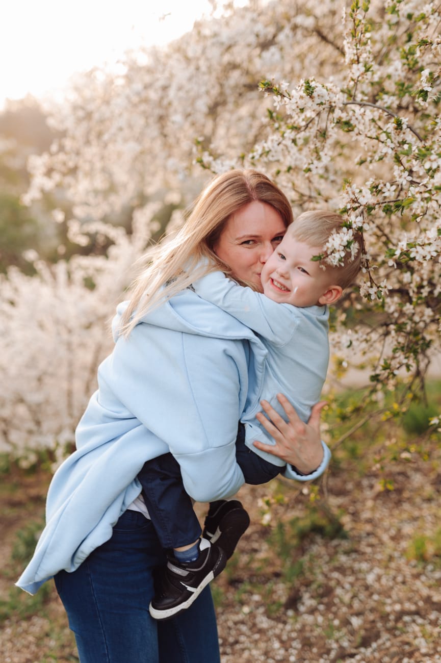 Mama całuje roześmianego syna kwitnące drzewa