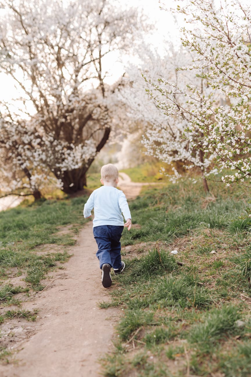 Chłopiec biegnący wśród kwitnących drzewek wiosennym popołudniem - rodzinna sesja zdjęciowa 