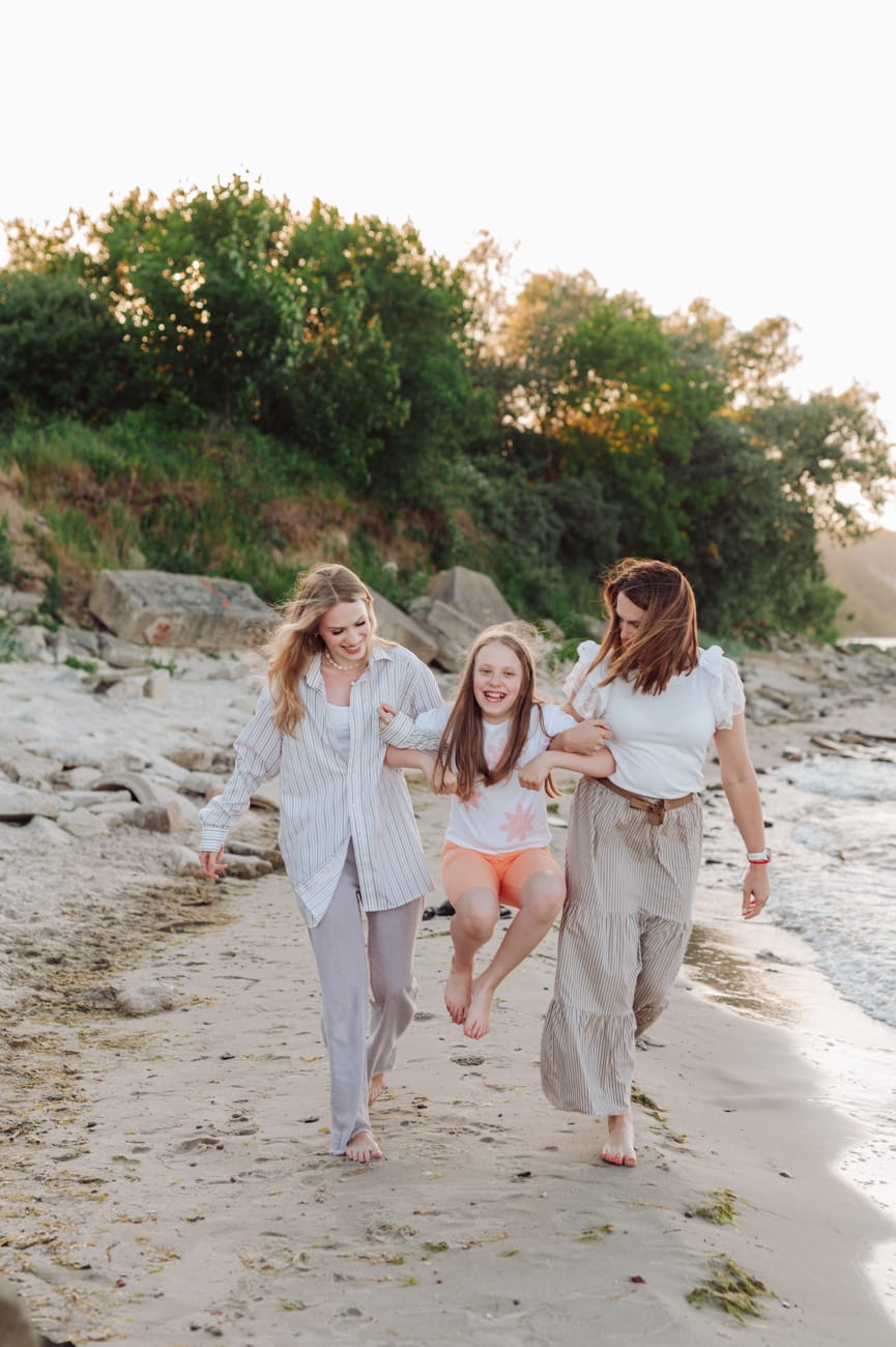 Mama idąca z córkami brzegiem morza o zachodzie słońca podczas nadmorskiej sesjiMama i córki spacer brzegiem morza sesja z nastolatkami