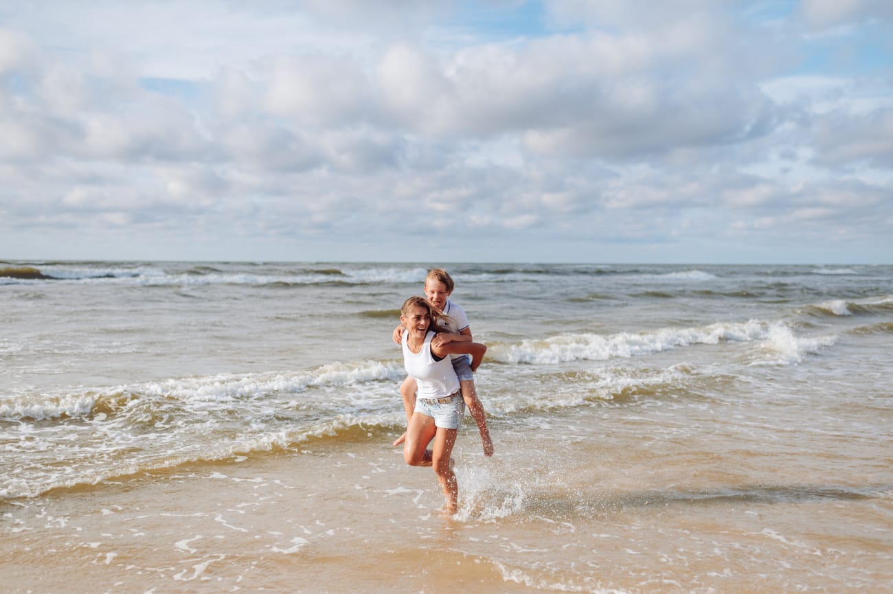 Mama z synem na barana biegną brzegiem morza sesja rodzinna 