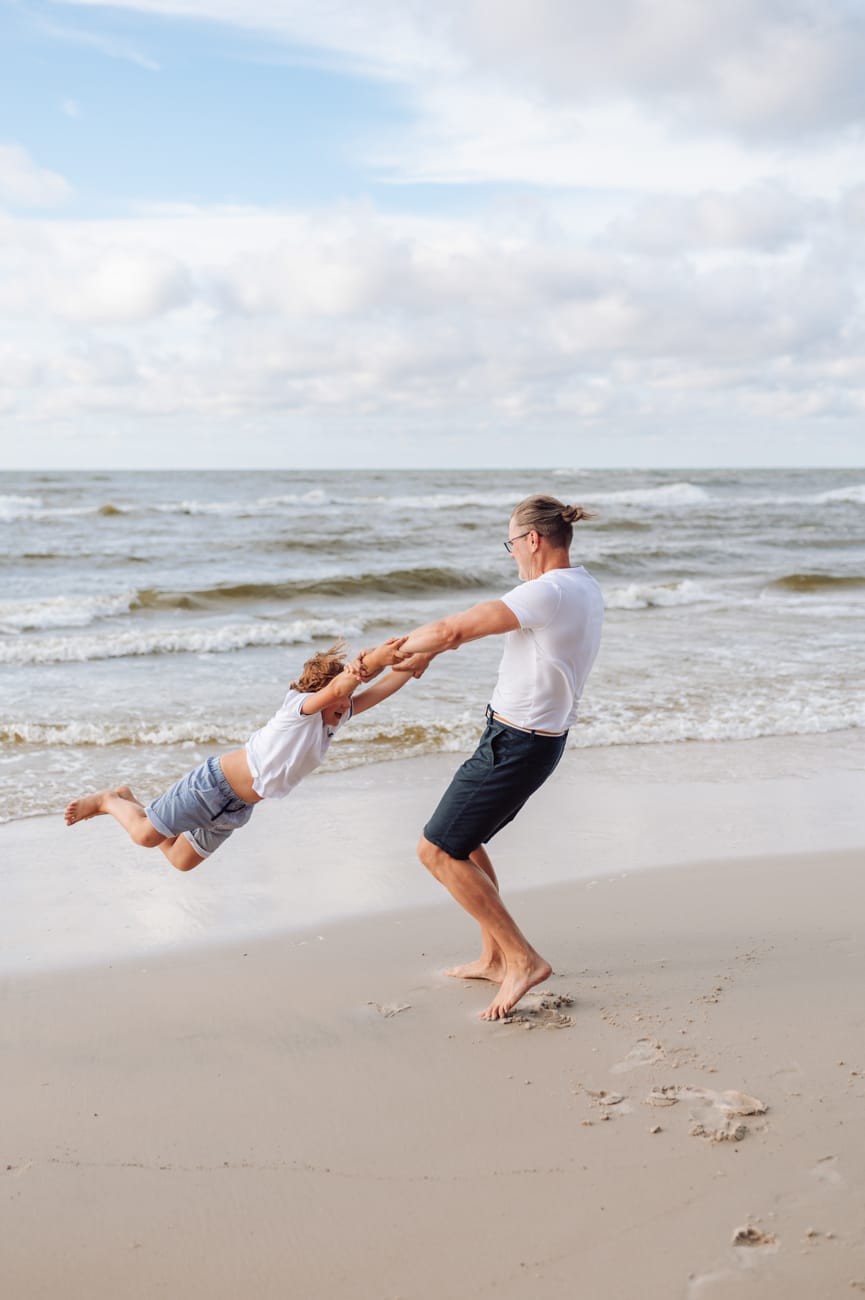 Tata kręcący się z synem na brzegu morza sesja rodzinna na plaży