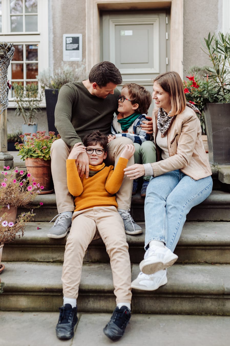 Rodzina z dwoma chłopcami siedzi na schodkach kamienicy podczas swobodnej miejskiej sesji z dziećmi w Gdańsku.