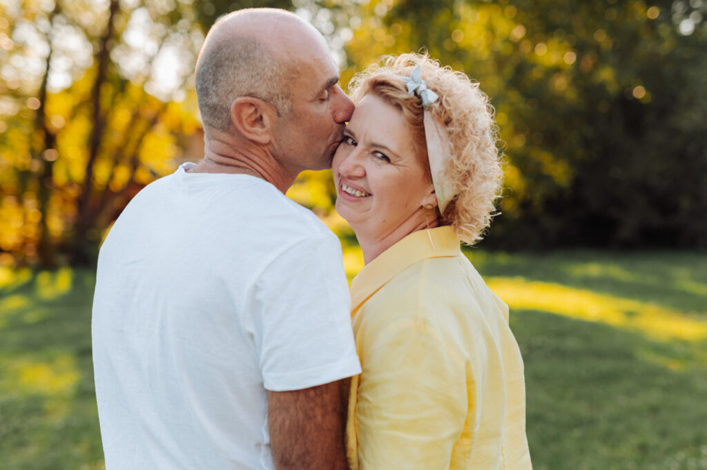 Mąż całuje żonę w policzek na łąkach na Kolibkach — sesja małżeńska Gdynia
