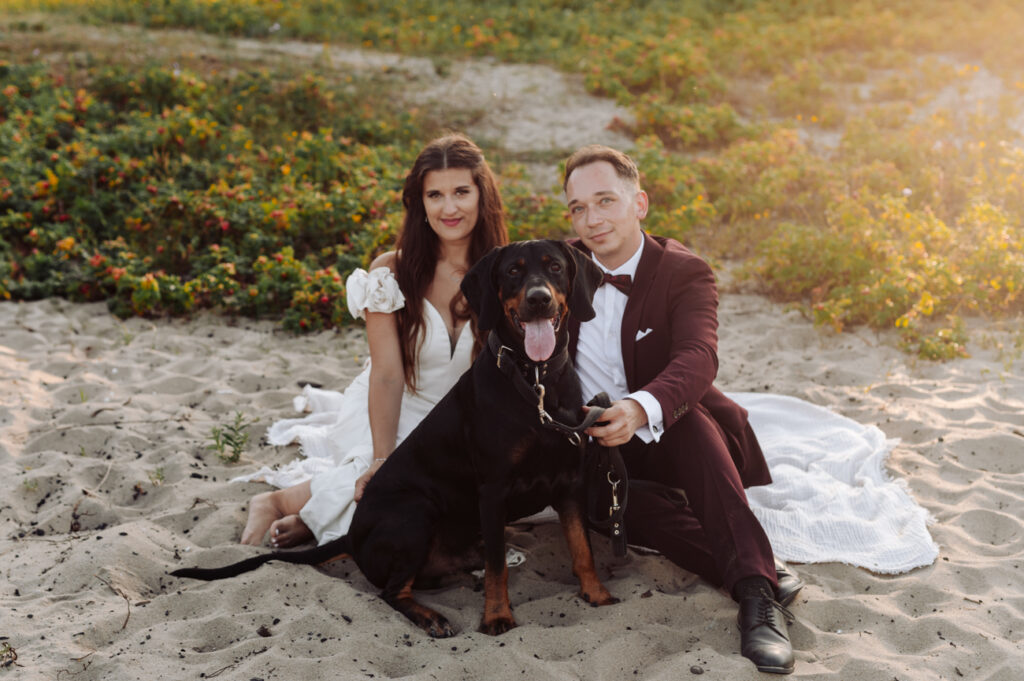 Para młoda z psem na plaży o zachodzie słońca — sesja poślubna Gdynia