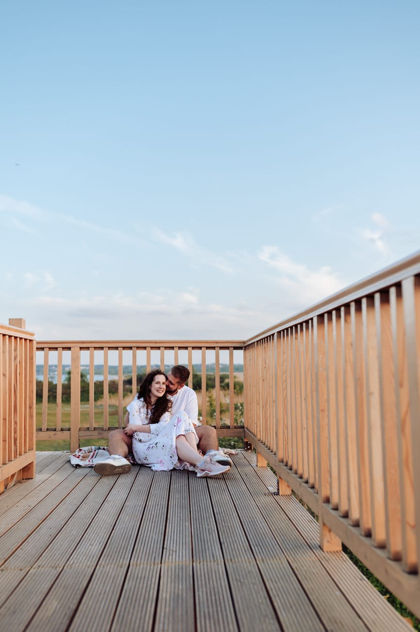 Para siedzi na drewniane kładce nad łąkami sesja narzeczeńska Rewa

