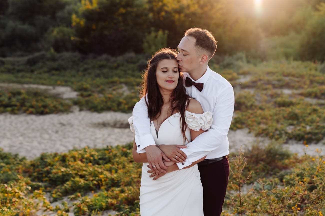 Nowożeńcy przytulają się na łące o zachodzie słońca sesja poślubna Trójmiasto
