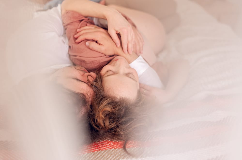 Para leżąca na łóżku i przytulająca się — domowa sesja ciążowa Gdańsk