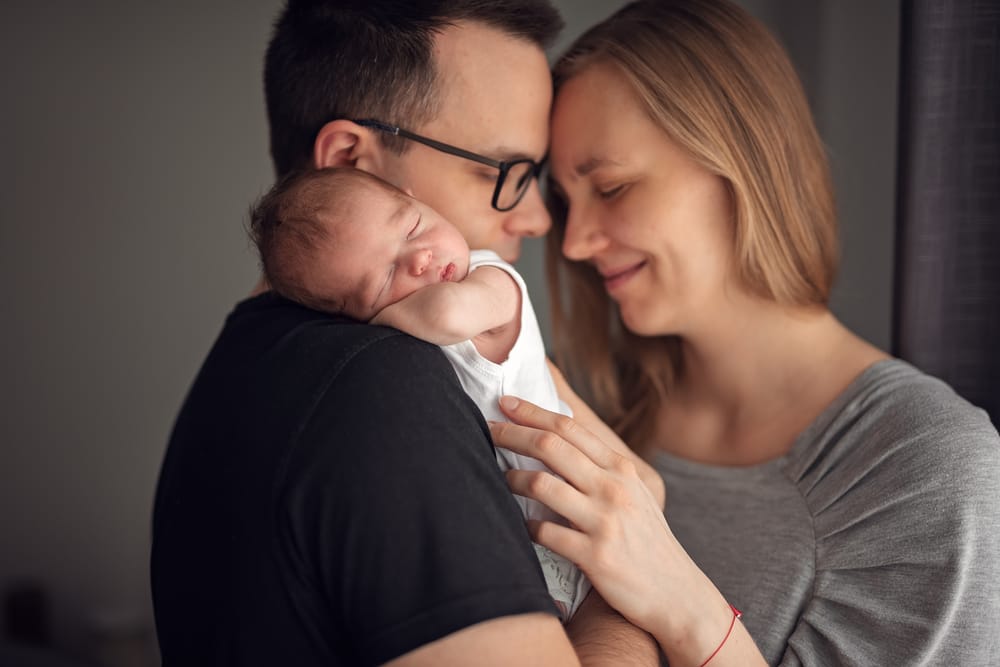 Jak przygotować dom do sesji noworodkowej rodzice z noworodkiem przy oknie