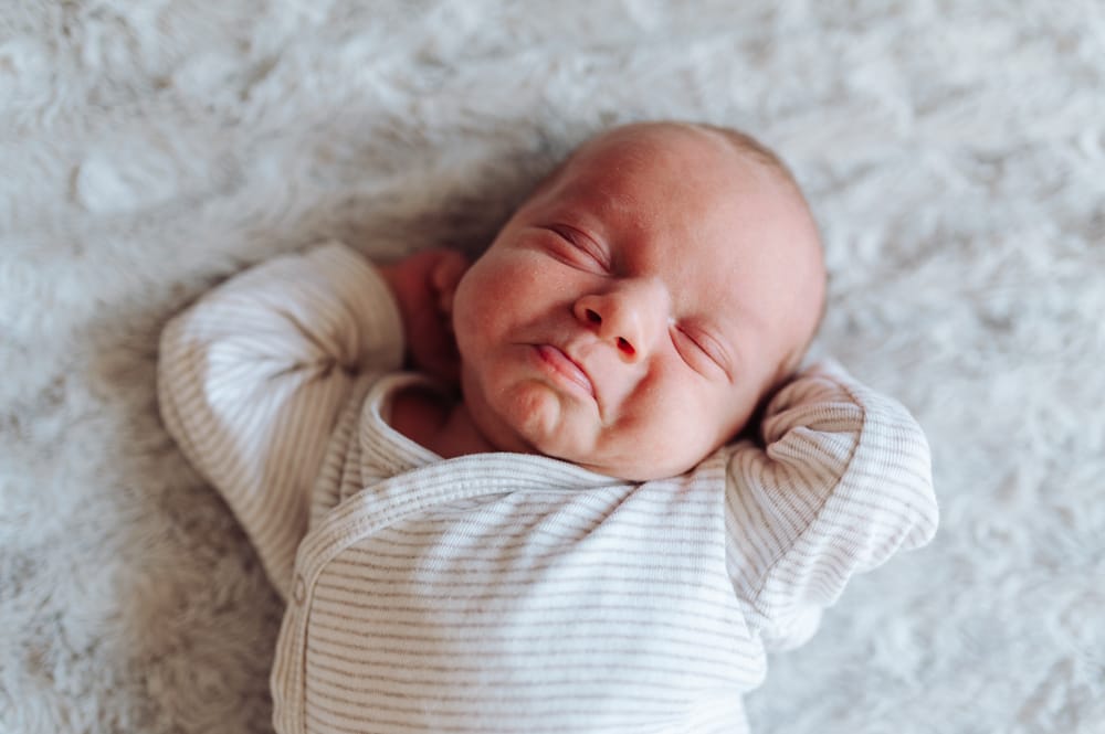 Noworodek przeciągający się i robiący charakterystyczną minę noworodka — sesja noworodkowa Gdańsk