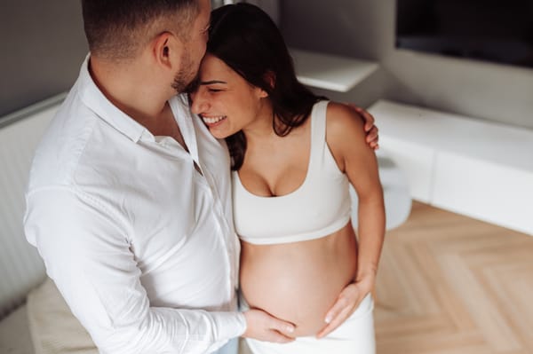 Roześmiana para przytulająca odsłonięty brzuszek — domowa sesja ciążowa Gdynia