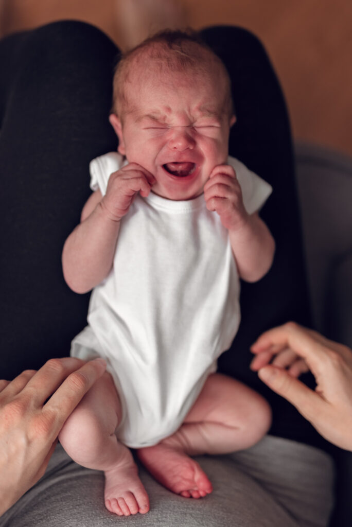 Płaczący noworodek na kolanach młodej mamy.