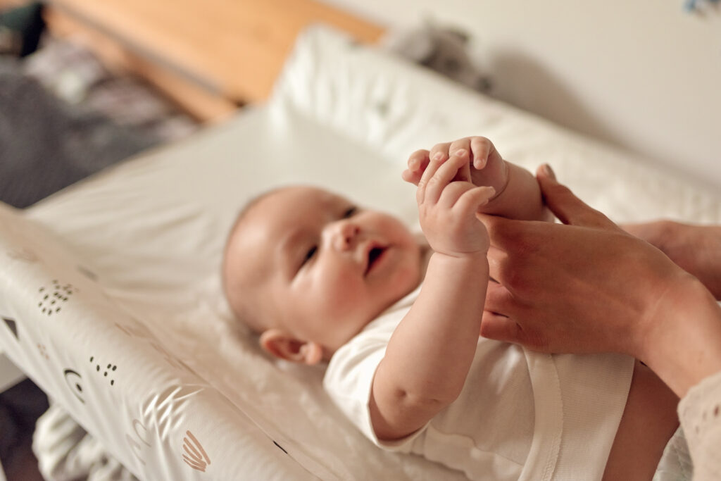 Niemowle leżące na przewijaku w trakcie szykowania do domowej sesji niemowlęcej.