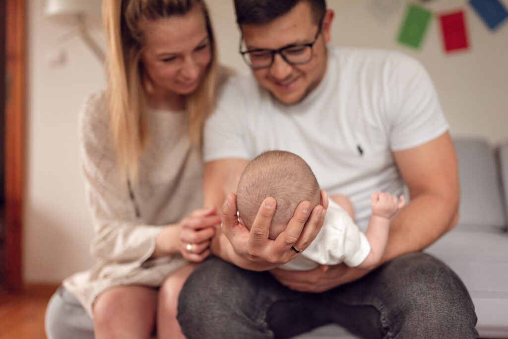 Rodzice wpatrujący się w swoje niemowle w trakcie domowej sesji niemowlęcej.