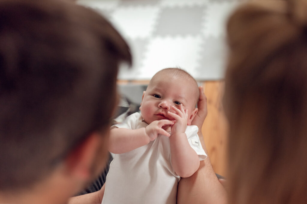 Portret niemowlęcia trzymanego między rodzicami w domowym zaciszu.