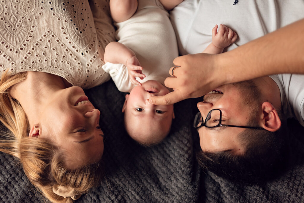 Niemowlę lezące między rodzicami, a tata dotyka jego noska.