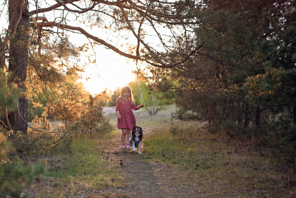 Dziewczynka z psem w leśnej scenerii o zachodzie słońca - rodzinna sesja ciązowa. 