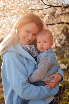 Szczęśliwa młoda mama bawi się ze swoim rocznym synem w parku w Gdyni, otoczeni kwitnącymi drzewami - profesjonalna fotografia rodzinna.