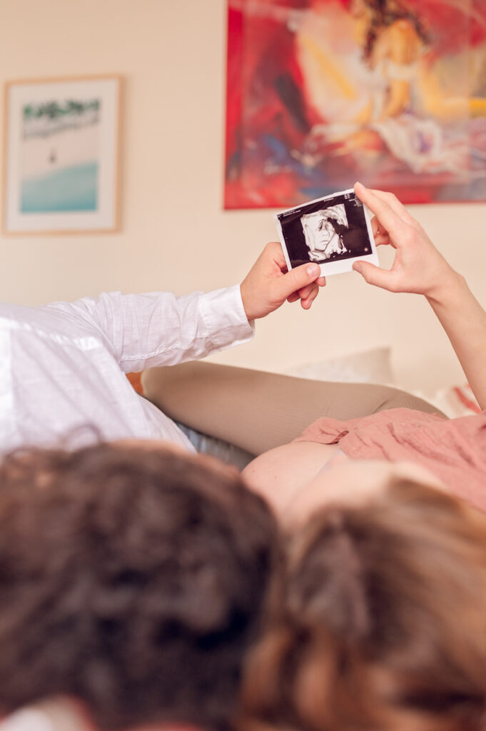 Przyszli rodzice wpatrujący się w zdjęcie USG swojego dziecka leżąc przytuleni na łóżku w swojej sypialni.