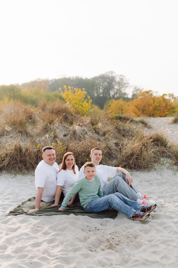 Portret rodziny z nastolatkami siedzącej na kocu na nadmorskiej plaży.