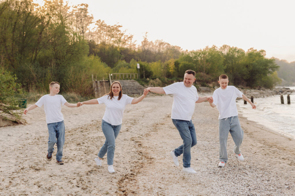 Rodzina radośnie bawiąca się na brzegu plaży podczas sesji zdjęciowej z nastoletnimi dziećmi.