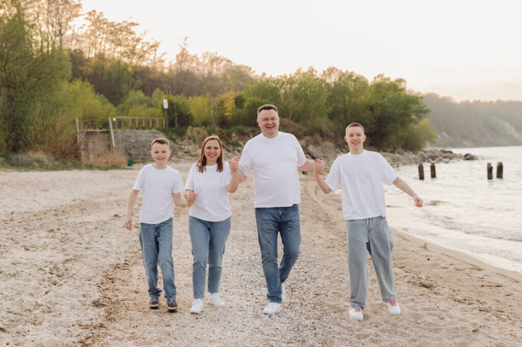 Rodzice z nastoletnimi dziećmi podczas rodzinnej sesji na plaży spacerują brzegiem morza. 