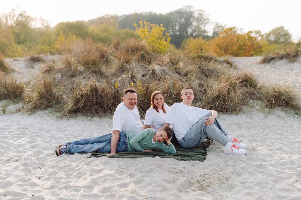 Rodzina z nastoletnimi chłopcami siedząca na kocu w nadmorskich trawach.